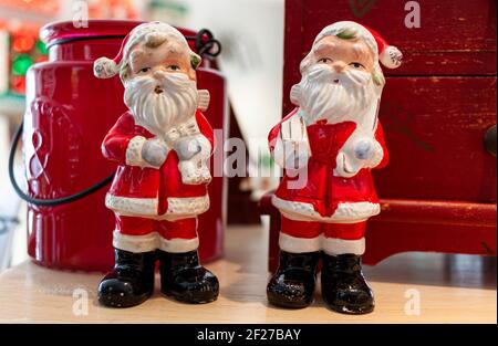 Nahaufnahme von zwei Weihnachtsmannpuppen aus Porzellan auf einem Holztisch. Dekorative Puppen stehen vor einer Vintage Kommode und einem ornamentalen ja Stockfoto