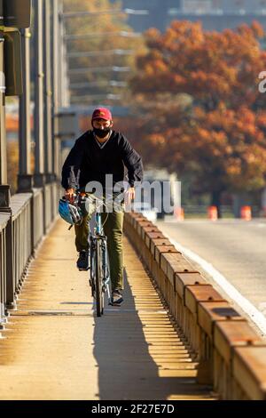 Washington DC, USA 11-06-2020: Ein Mann pendelt zur Arbeit auf seinem Fahrrad. Er fährt auf der Theodore Roosevelt Bridge über den Potomac River. Es hat einen Narro Stockfoto