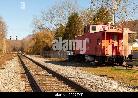 Clifton, VA, USA 11/14/2020: View of the train tracks, ballast, track sleepers and an abandoned red caboose passenger train cabin in front of historic Stockfoto