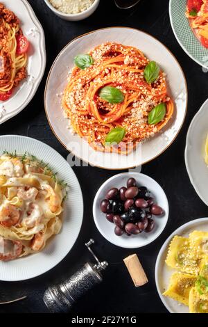 Italienisches Essen, von oben auf schwarzem Hintergrund aufgenommen. Spaghetti mit Basilikum, Oliven, Weinkorken, Ravioli Stockfoto