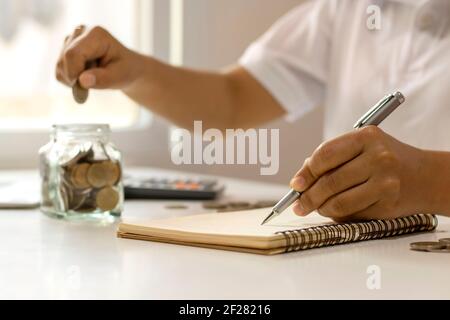 Geld sparen Idee. Eine Frauenhand hält einen Stift, um die Ausgaben im Haus zu notieren. Stockfoto