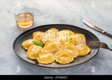Ein Teller gekochter italienischer Ravioli, garniert mit frischen Basilikumblättern, mit einem Glas Weißwein Stockfoto