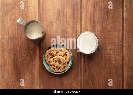 Chocolate Chip Cookies auf einem dunklen rustikalen Holzhintergrund, von oben mit einem Milchkännchen und Glas geschossen Stockfoto