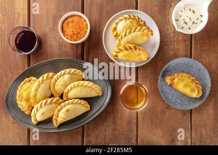 Empanadas mit Saucen und Wein, von oben auf einem rustikalen Holzhintergrund geschossen Stockfoto