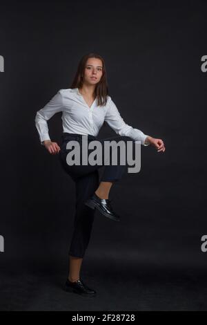 Braunhaarige Frau mit langen Haaren, in blauer Jeans, weißem Hemd, auf schwarzem Hintergrund Stockfoto