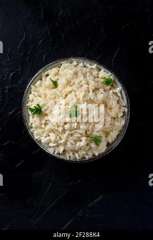 Weißer Reis, gekocht, mit Petersilie, oben auf schwarzem Hintergrund geschossen Stockfoto