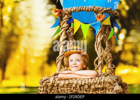 Kleiner lockiger Junge in der Luft, der träumt, schaut in den Himmel. Baby in einem Ballonkorb. Stockfoto