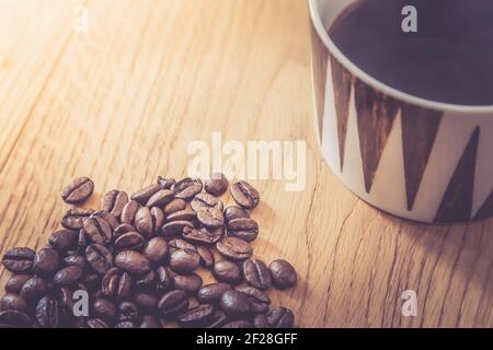 Nahaufnahme von frisch gerösteten Kaffeebohnen und Kaffeebecher Auf Holzhintergrund Stockfoto