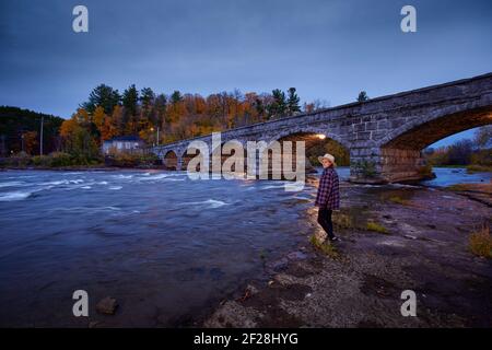 Junge Frau, die am Ufer in der Nähe der Steinbögen der Pakenham Bridge über den Mississippi River in Ontario steht. Stockfoto