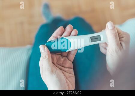 Frau im mittleren Alter sitzt auf dem Bett und überprüft den Schwangerschaftstest. Ergebnis positiv, â € œSchwangerâ € Stockfoto