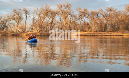 Älterer Rüde paddelt ein aufblasbares Packraft auf einer ruhigen see mit Reiher Rookery im frühen Frühjahr im Norden von Colorado Stockfoto