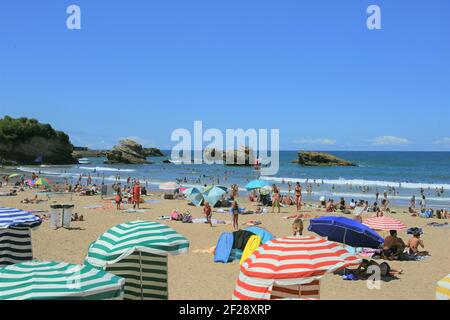 Biarritz, Französisch Baskenland, Frankreich - Strandgänger unter bunten Sonnenschirmen am La Grande Plage, dem größten Strand der Stadt. Stockfoto