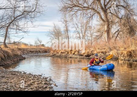 Älterer Rüde paddelt ein aufblasbares Packfloß auf einem Fluss Im Frühjahr - Poudre River im Norden von Colorado Stockfoto