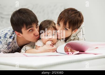 Glückliche junge Familie mit kleinen Mädchen ein Buch zu lesen Auf dem Bett Stockfoto