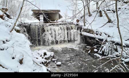 Winterlandschaft mit Waldfluss. Tal der Wasserfälle. Schneebedeckte Bäume am Flussufer. Ein untergetauchte Baumstamm im Fluss. Winterlandschaft Stockfoto