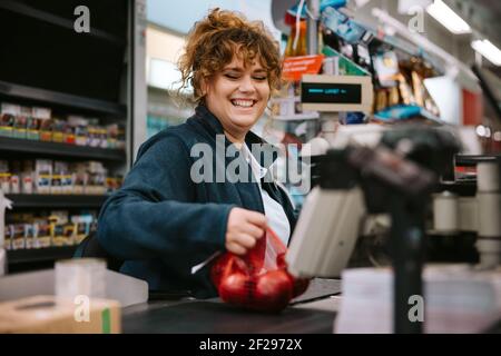 Weibliche Kassiererin, die die Produkte an der Kasse im Supermarkt durch den Barcode-Leser führt. Frau, die an der Kasse des Lebensmittelladens arbeitet. Stockfoto