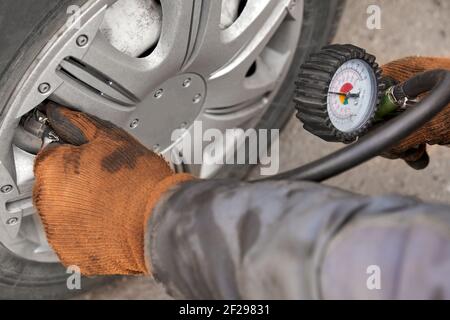 Mechaniker an der Reparaturwerkstatt, Reifendruck mit Manometer prüfen. Nahaufnahme, selektiver Fokus Stockfoto