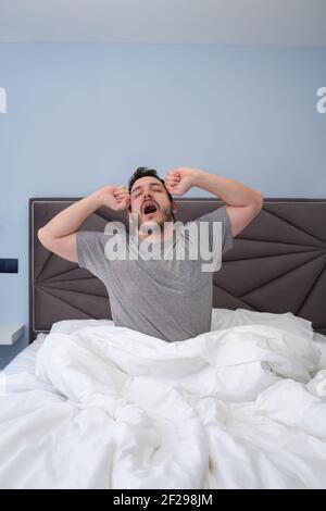 Junger lateinischer Mann, der sich nach dem Schlafen im Bett ausdehnt und gähnt. Am späten Vormittag. Stockfoto