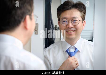 Ein asiatischer Geschäftsmann mittleren Alters lächelt, während er den Spiegel anschaut Am Morgen Stockfoto