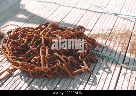 Rostige Kette in einem Haufen im Sonnenlicht, draußen auf Holzboden Stockfoto