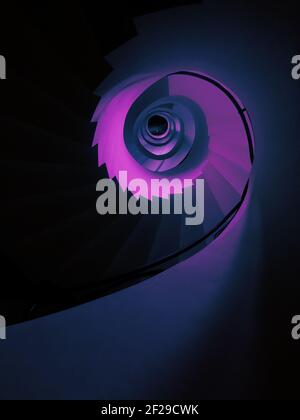 Eine vertikale Aufnahme einer hohen Wendeltreppe in einem niedrigen Winkel In ästhetischer lila Farbe Stockfoto