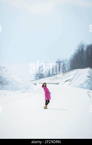 Eine vertikale Aufnahme einer stylischen Frau, die ein Rosa trägt Mantel und Posen in einem Winterwald Stockfoto