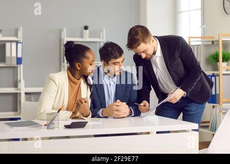 Bankangestellter gibt einem kaukasischen Mann und seiner dunkelhäutigen Frau Dokumente zur Unterschrift. Stockfoto