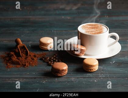 tasse Kaffee, Kaffeebohnen, gemahlener Kaffee und Makronen auf Holzhintergrund Stockfoto