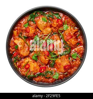 Huhn Vindaloo mit Spinat in schwarzer Schüssel isoliert auf weiß. Indische Küche Fleisch Chili Curry Gericht. Authentisches asiatisches Essen. Stockfoto