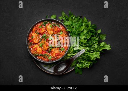 Huhn Vindaloo mit Spinat in schwarzer Schale auf dunkler Schieferplatte. Indische Küche Fleisch Chili Curry Gericht. Authentisches asiatisches Essen. Draufsicht Stockfoto