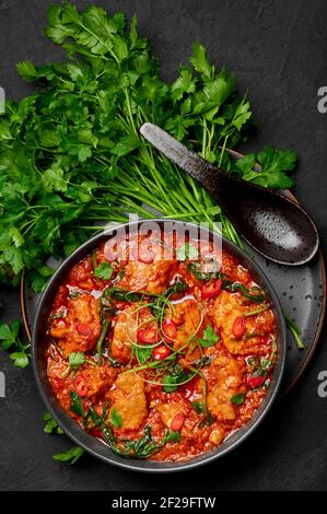 Huhn Vindaloo mit Spinat in schwarzer Schale auf dunkler Schieferplatte. Indische Küche Fleisch Chili Curry Gericht. Authentisches asiatisches Essen. Draufsicht Stockfoto