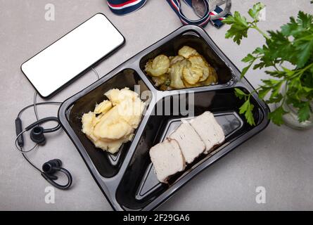 Draufsicht der Lunchbox mit gesunden nahrhaften Lebensmitteln und Smartphone am Arbeitsplatz auf grauem Hintergrund Stockfoto