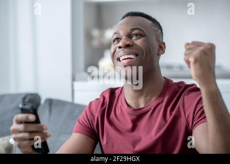 Ein dunkelhäutiger junger Mann, der Fernsehen schaut und aufgeregt schaut Stockfoto