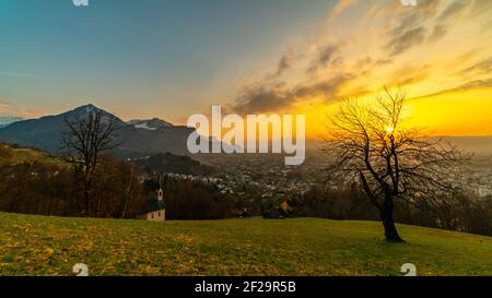 Schöner Sonnenuntergang und Nachglühen in Dornbirn mit Wolken, die auf die Rhomberkapelle zeigen, farbiger Himmel über Rheintal, Staufenspitze, Säntis Stockfoto