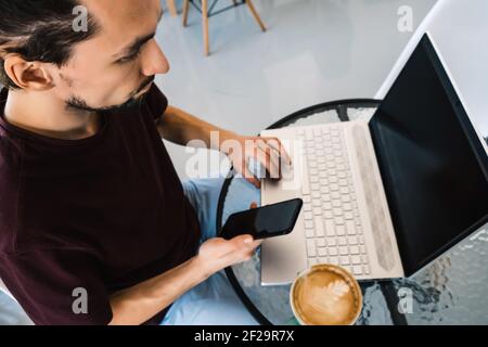 Freiberuflicher Mann, der mit Laptop und Smartphone im Café arbeitet. Draufsicht. Stockfoto