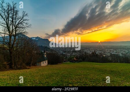 Schöner Sonnenuntergang und Nachglühen in Dornbirn mit Wolken, die auf die Rhomberkapelle zeigen, farbiger Himmel über Rheintal, Staufenspitze, Säntis Stockfoto