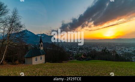 Schöner Sonnenuntergang und Nachglühen in Dornbirn mit Wolken, die auf die Rhomberkapelle zeigen, farbiger Himmel über Rheintal, Staufenspitze, Säntis Stockfoto