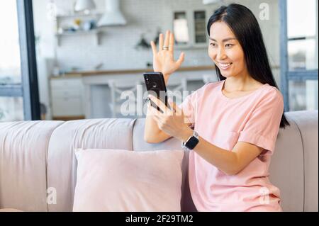 Junge asiatische Mixed-Race Erwachsene weibliche Blogger Streaming-Video online über Handy aus dem Wohnzimmer, Aufnahme Tutorial für Social Media-Netzwerk, winken, Gruß Freund mit High-Five, zu sagen, hallo Stockfoto