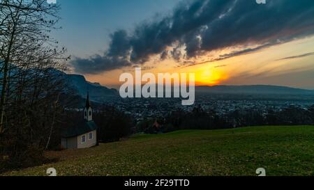 Schöner Sonnenuntergang und Nachglühen in Dornbirn mit Wolken, die auf die Rhomberkapelle zeigen, farbiger Himmel über Rheintal, Staufenspitze, Säntis Stockfoto