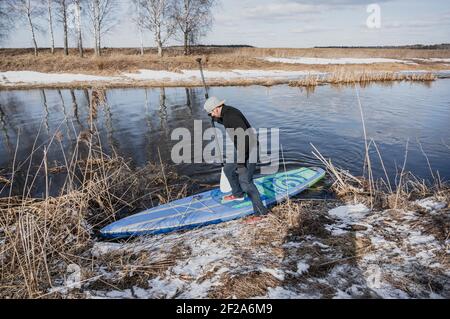 Ein Mann steht auf einem aufblasbaren Brett mit einem Paddel, Paddleboarding im Winter Stockfoto