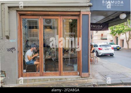 Blick von außen auf eine Person, die neben einem Fenster in einem Eckcafe (Café) in Newtown, Sydney, Australien sitzt Stockfoto