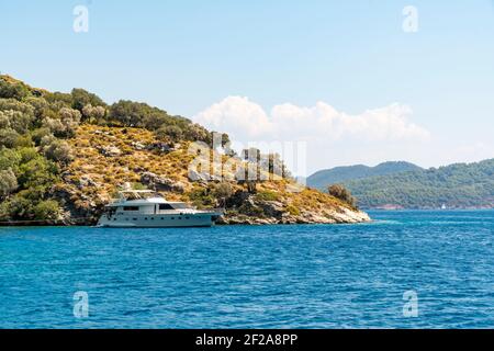 Sommerkonzept: Luxuriöses weißes Yacht Boot verankert Heck in einer Bucht mit blau türkisfarbenem Wasser. Blick vom Land mit grünen Bäumen und Meer im Hintergrund Stockfoto