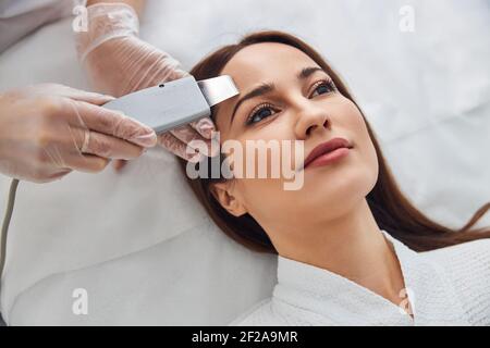 Kosmetologe Reinigung der weiblichen Stirn mit Ultraschall-Scrubber Stockfoto
