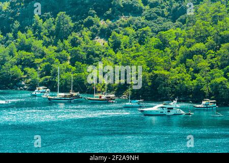 Sommerkonzept: Viele türkische Schluchten und einige weiße Luxusyachten vor der Ägäis mit Sonnenstrahl im Hintergrund vor Anker. Natur mit Kopierbereich Stockfoto