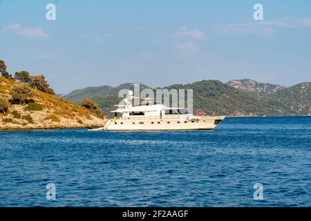 Sommerkonzept: Luxuriöses weißes Yacht Boot verankert Heck in einer Bucht mit blau türkisfarbenem Wasser. Blick vom Land mit grünen Bäumen und Meer im Hintergrund Stockfoto