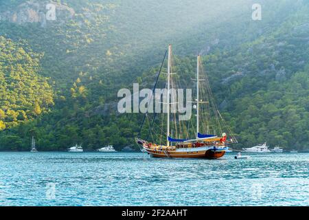 Sommerkonzept: Eine türkische Gulet Yacht, die an der Ägäis mit Sonnenstrahl im Hintergrund verankert ist. Natürliches Foto mit Kopierbereich. Grüner und blauer Kontrast Stockfoto