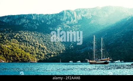 Sommerkonzept: Eine türkische Gulet Yacht, die an der Ägäis mit Sonnenstrahl im Hintergrund verankert ist. Natürliches Foto mit Kopierbereich. Grüner und blauer Kontrast Stockfoto