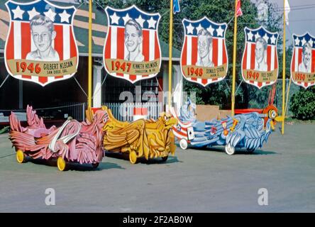 Bunte Speckbox-Autos standen 1964 auf der Rennstrecke in Derby Downs, Akron, Ohio, USA, in der Box. Der Veranstaltungsort war die Heimat des ‘All American Soap Box Derby’, da es als Works Progress Administration (WPA) Projekt im Jahr 1930s gebaut wurde. Traditionen gibt es reichlich mit berühmten früheren Gewinnern der Rennen in der 1940s auf Transparenten gezeigt, darunter Gilbert Kegan (1946), Keith Holmboe (1947), Donald Strub (1948) und Fred Derks (1949). Dieses Bild stammt von einem alten amerikanischen Amateur Kodak Farbtransparenz - ein Vintage 1960s Foto. Stockfoto