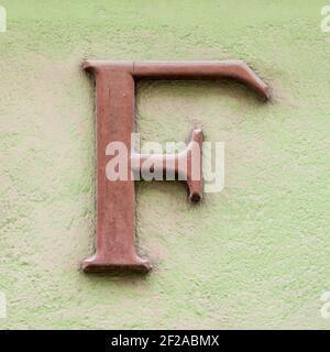 Brauner Buchstabe F mit Serifen an grüner Hauswand Stockfoto