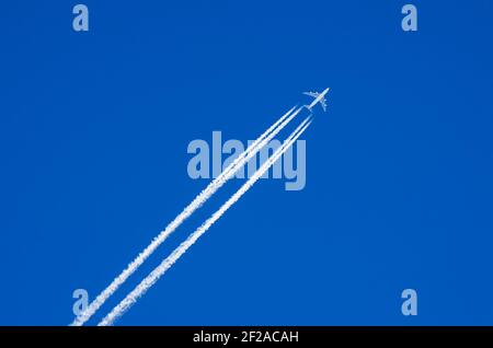 Weißes Flugzeug fliegt in den blauen Himmel und hinterlässt einen Contrails Dahinter Stockfoto